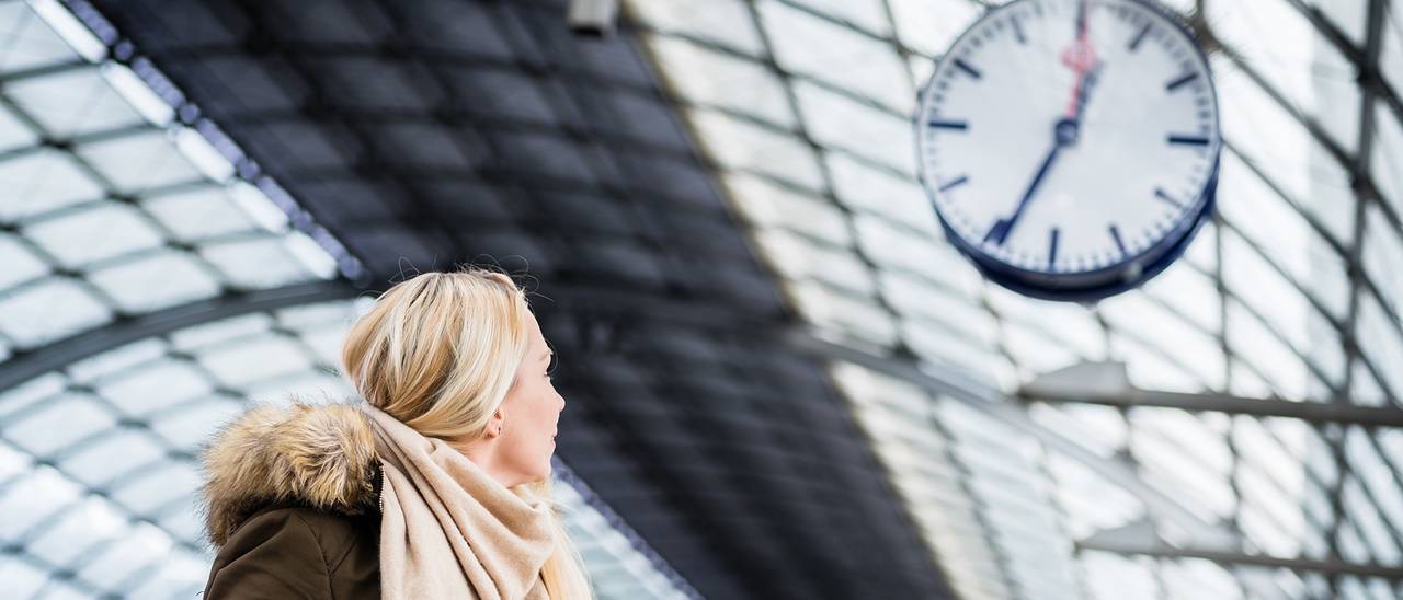 Eine Frau am Bahnhof schaut auf eine Uhr von Bürk.